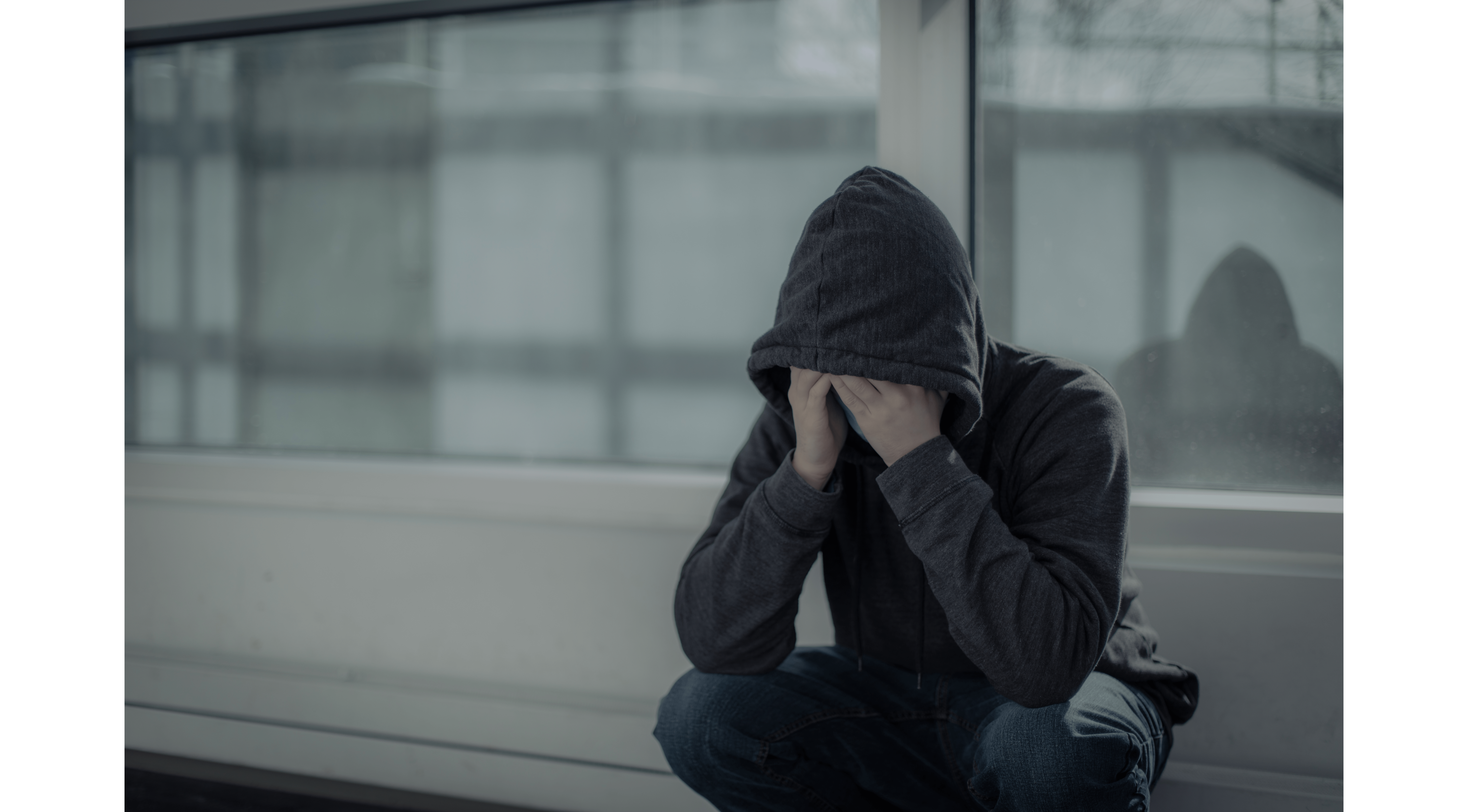 Persona joven cubriéndose la cara con las manos y una capucha
