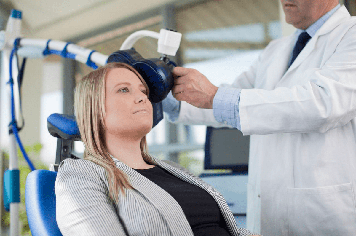 mujer sentada recibiendo estimulación con un aparato en el lado izquierdo de su cerebro